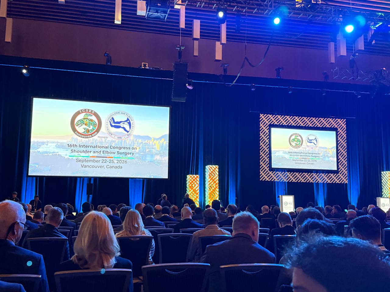The congress hall in Vancouver, with delegates seated facing the stage and two large screens.