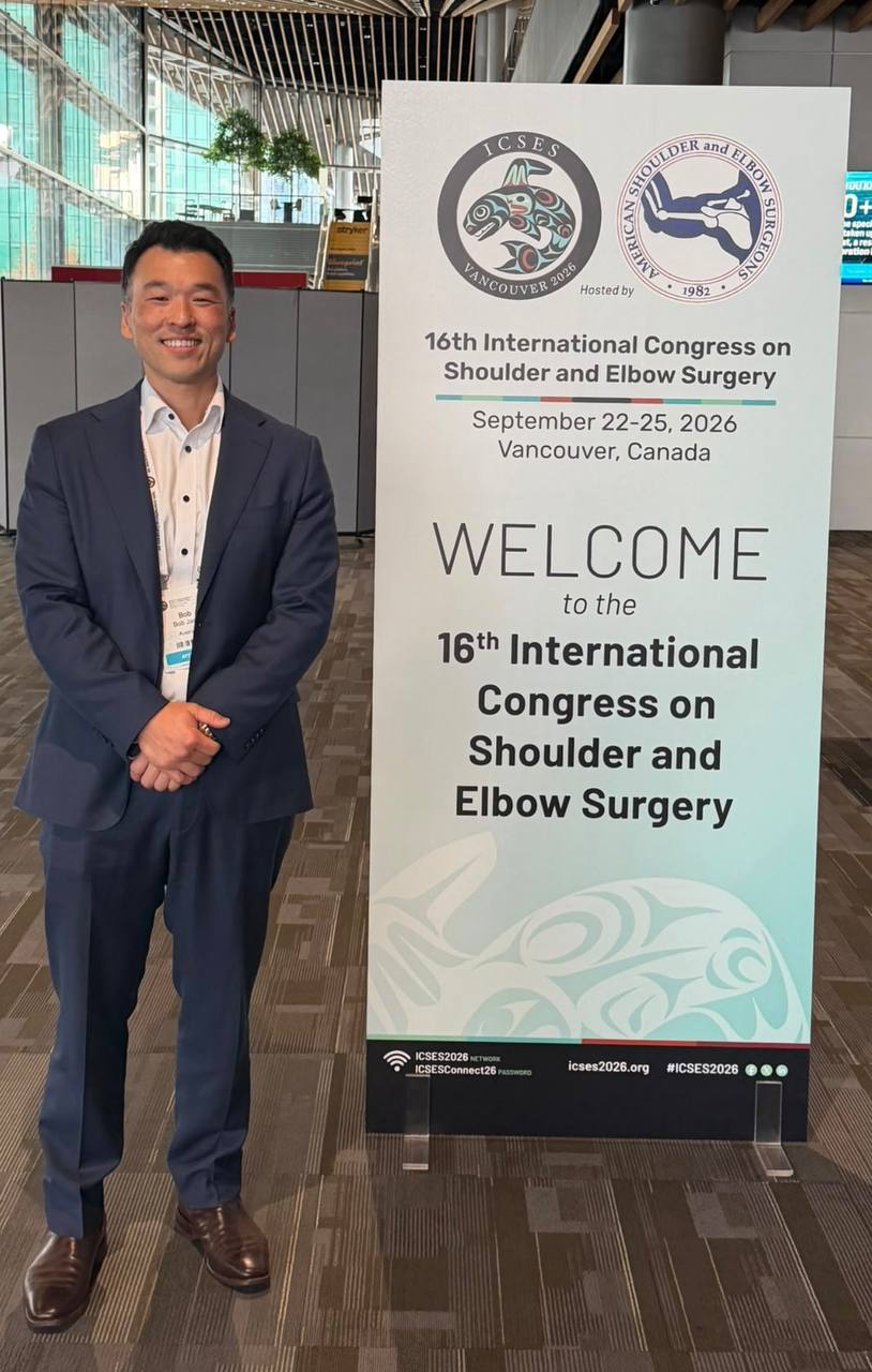 Dr Bob Jang standing beside the welcome banner for the International Congress on Shoulder and Elbow Surgery in Vancouver.