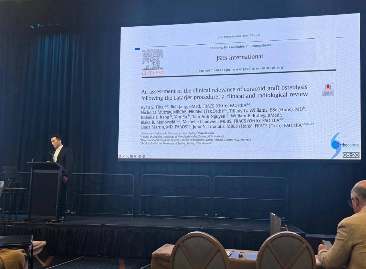 Dr Bob Jang presenting at a conference, with a slide behind him.