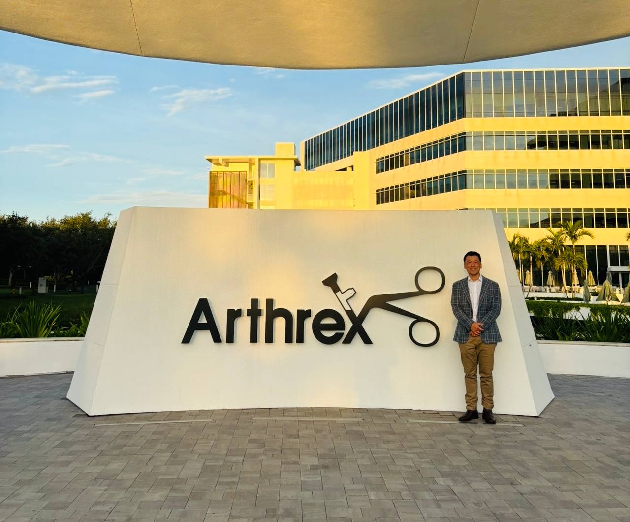 Dr Bob Jang standing beside the Arthrex sign at the Arthrex headquarters in Naples, Florida.