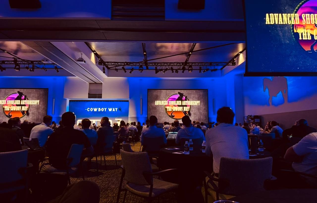A darkened lecture hall with delegates seated facing screens for the Advanced Shoulder Arthroscopy course, The Cowboy Way.