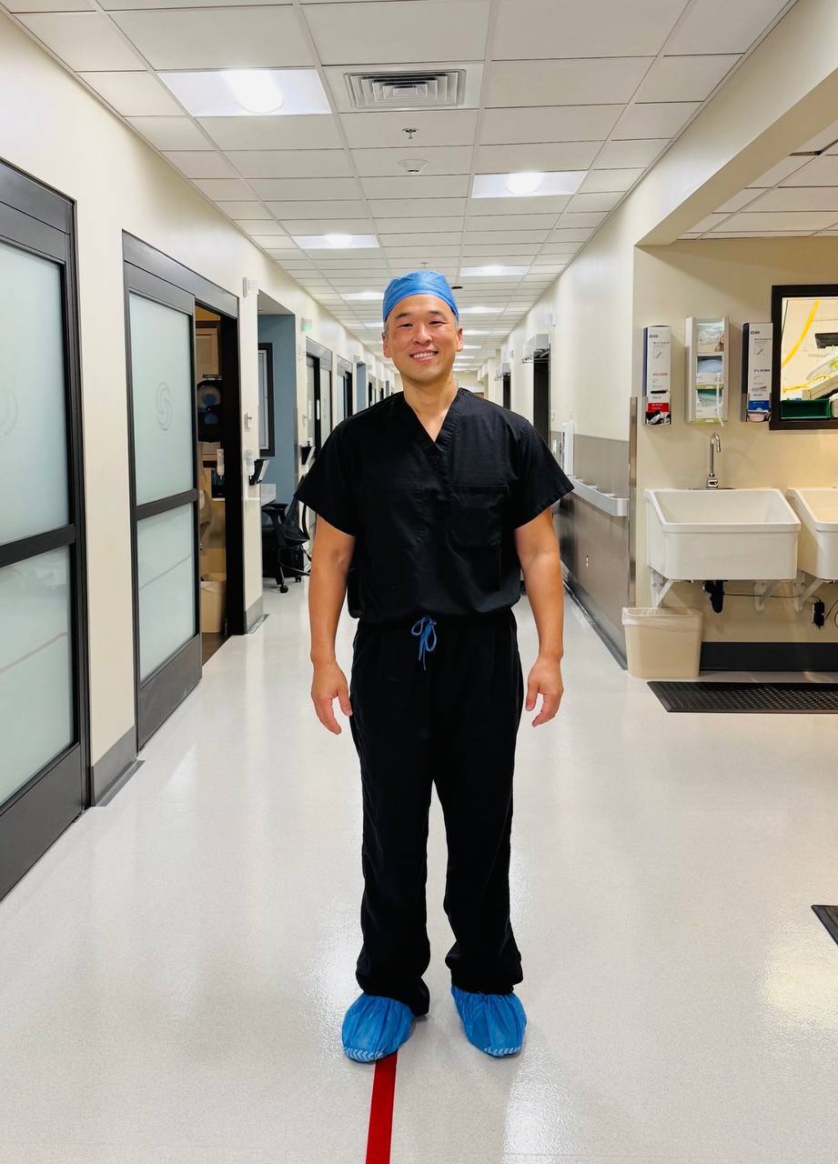 Dr Bob Jang in scrubs and a surgical cap, standing in a theatre corridor.